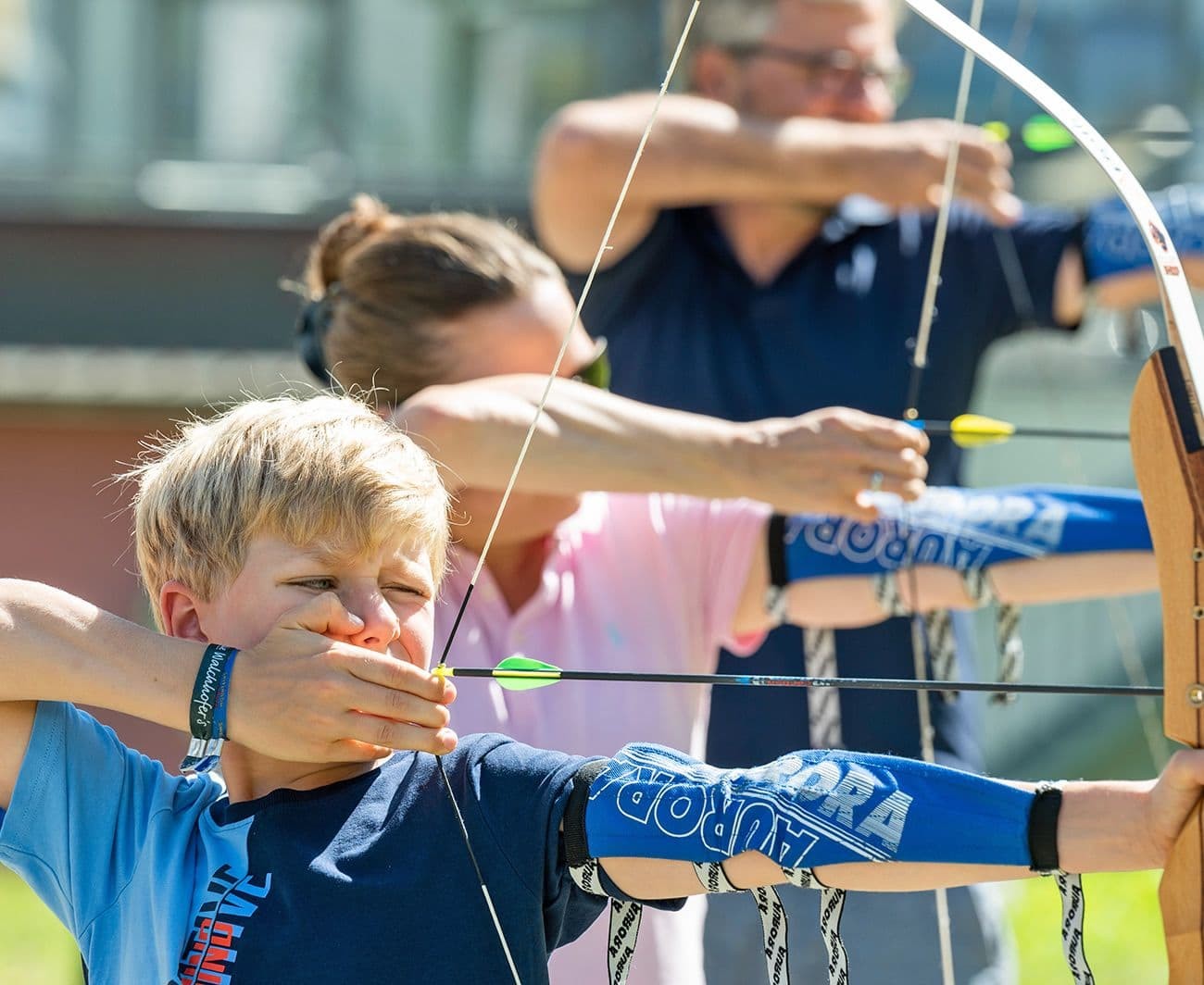 Three people aiming bows during an archery session outdoors