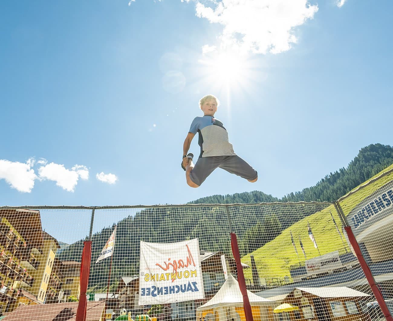 Child jumping on a trampoline with a sunny mountain backdrop