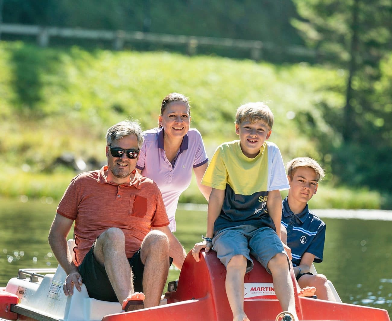 A family of four enjoys a sunny day on a pedal boat by the lake
