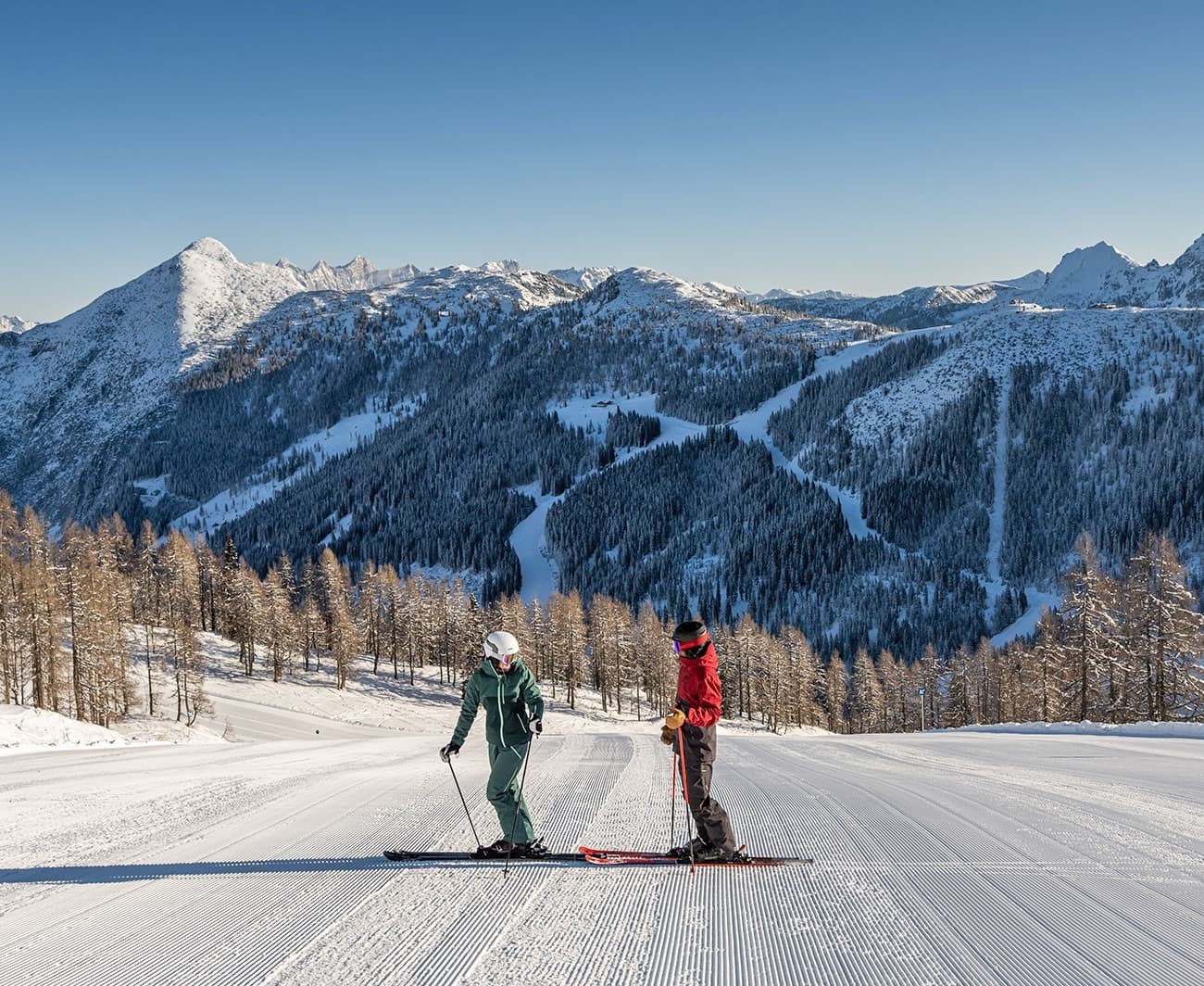 Two skiers on a snowy slope with a mountainous background