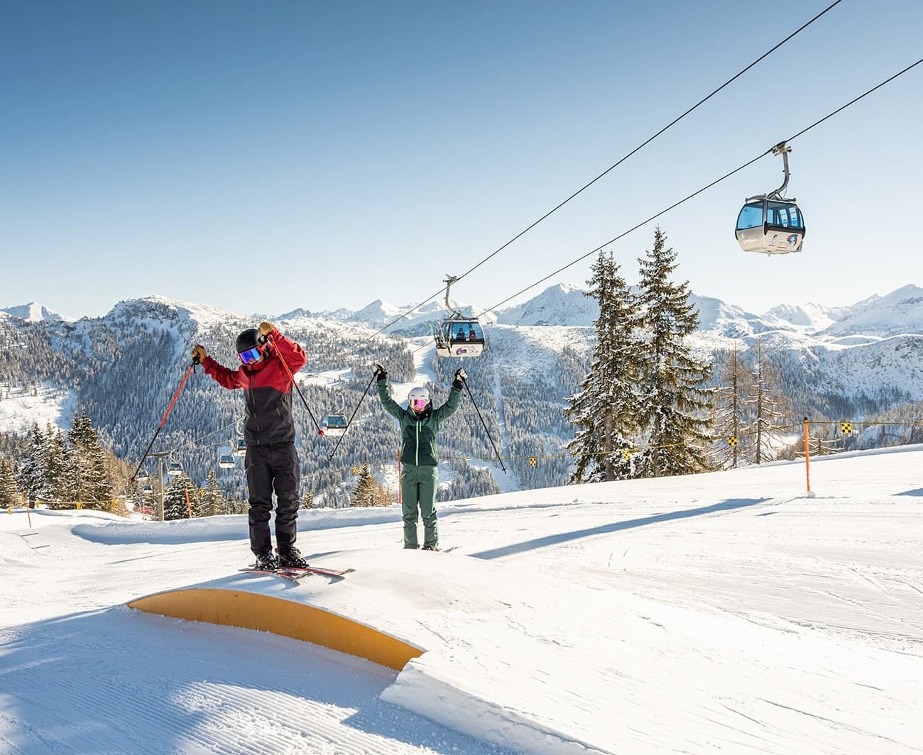 Skiers enjoy a snowy mountain slope with a clear blue sky and cable cars above