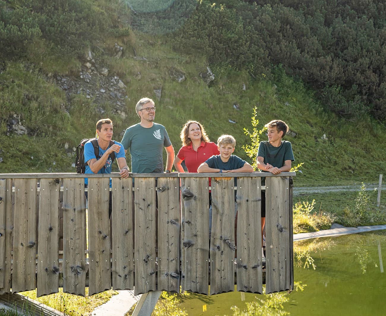 A group of five people standing on a wooden bridge in a sunny, green landscape