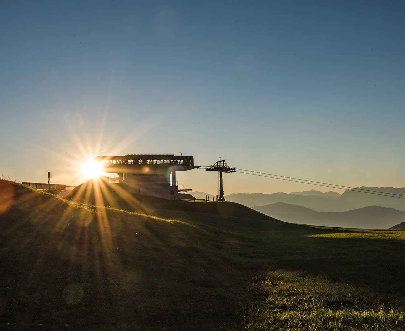 Sunrise behind a ski lift station with mountain silhouettes in the distance