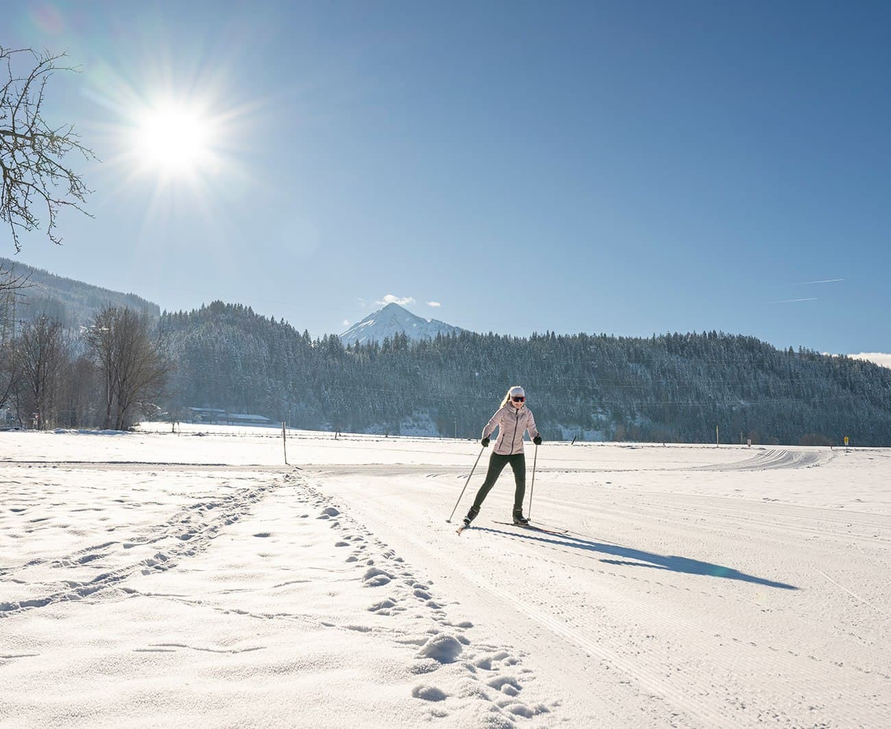 A person cross-country skiing on a sunny, snow-covered landscape with mountains in the background